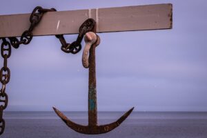 Rostiger Bootsanker mit Kette vor ruhiger See und violettem Himmel